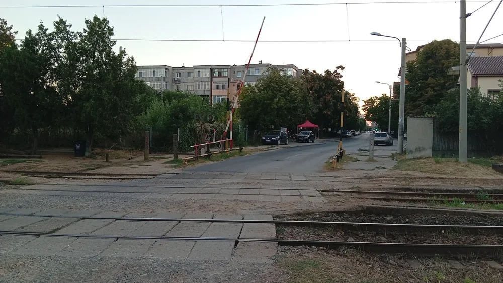 The level crossing at Bordei, west of the station — hand-worked barriers, concrete panels, and the city carrying on across the tracks