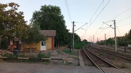 A crossing keeper’s hut beside the electrified railway west of Craiova station, the line curving away east at dusk
