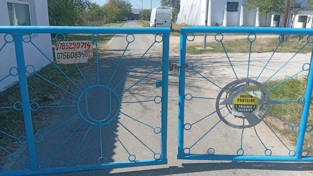 The road gate — chained and signed as a guarded site, with the contact number for the field painted on the board