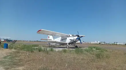A white An-2 biplane parked on the concrete apron at Balta Verde airfield, Craiova