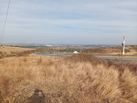 Dry grass on a hilltop above hairpin bends with guard rails, Craiova spread across the horizon with its white stadium