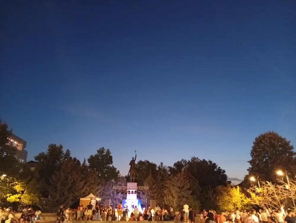 A stage set up below the equestrian statue, crowd gathered at dusk