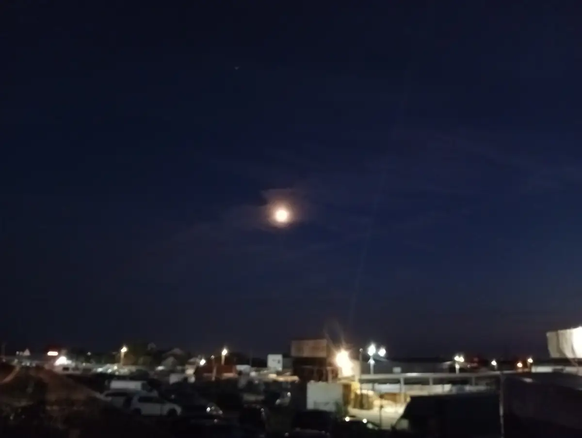 The moon over lit yards and parked cars at the edge of town, 19 September 2026. Spot not yet named
