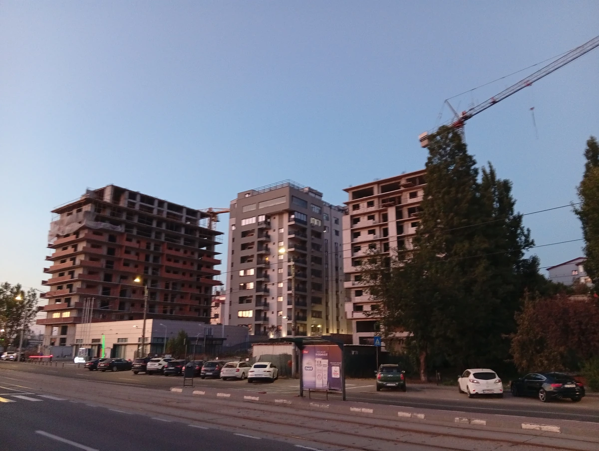 New apartment towers under construction by a tram line in Craiova at dusk, a tower crane above them, 20 September 2026