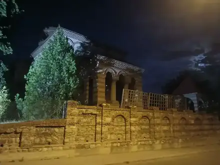 A brick and stone church behind its walled yard in Craiova at night, lit by a street lamp