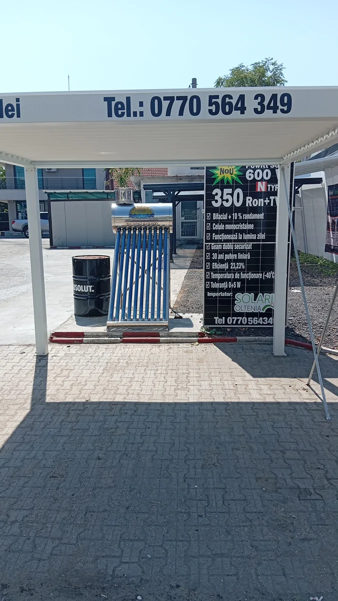 An open-air solar showroom: aluminium pergola, evacuated-tube water heater, a 600 W panel used as its own price board