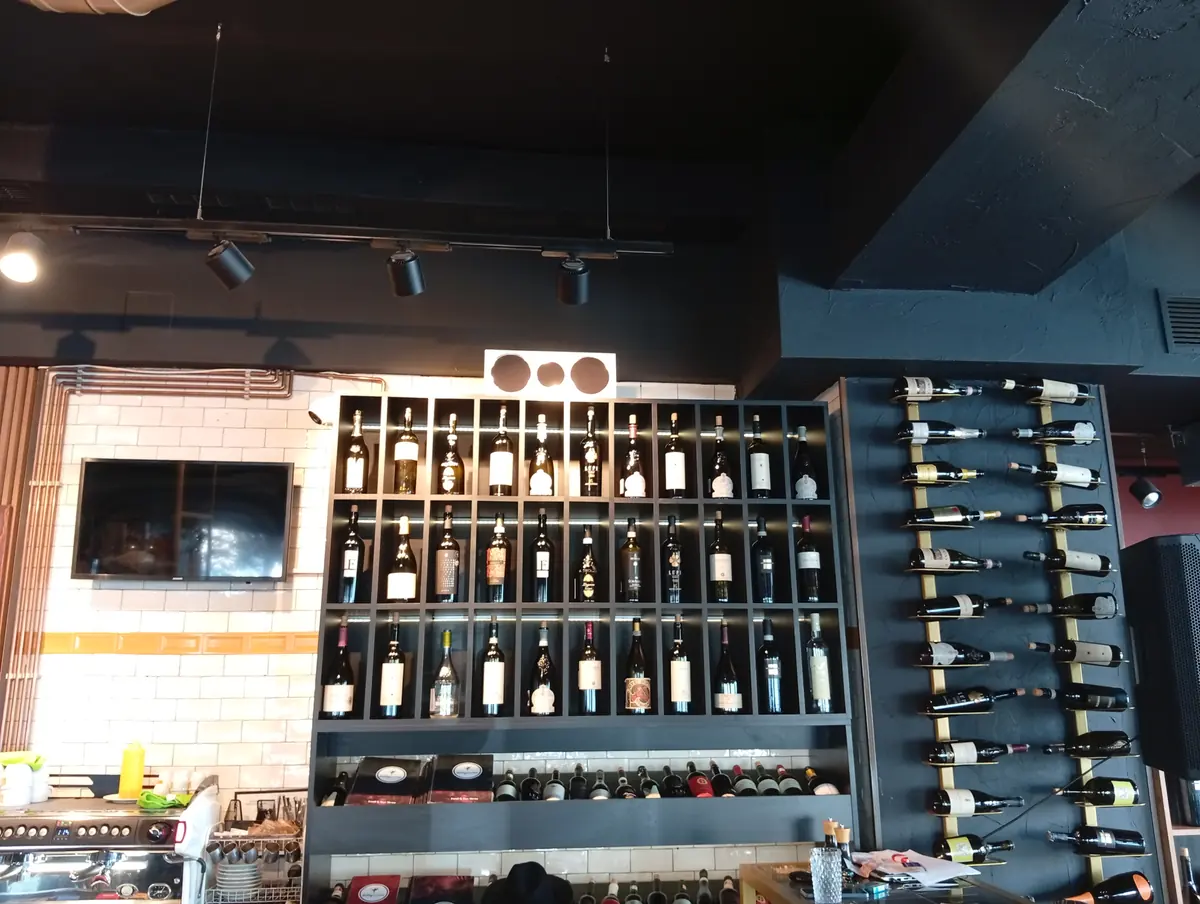 Restaurant bar in Craiova: a wall of wine bottles in lit black cubbies and on brass wall racks, white tiles and an espresso machine, 22 September 2026