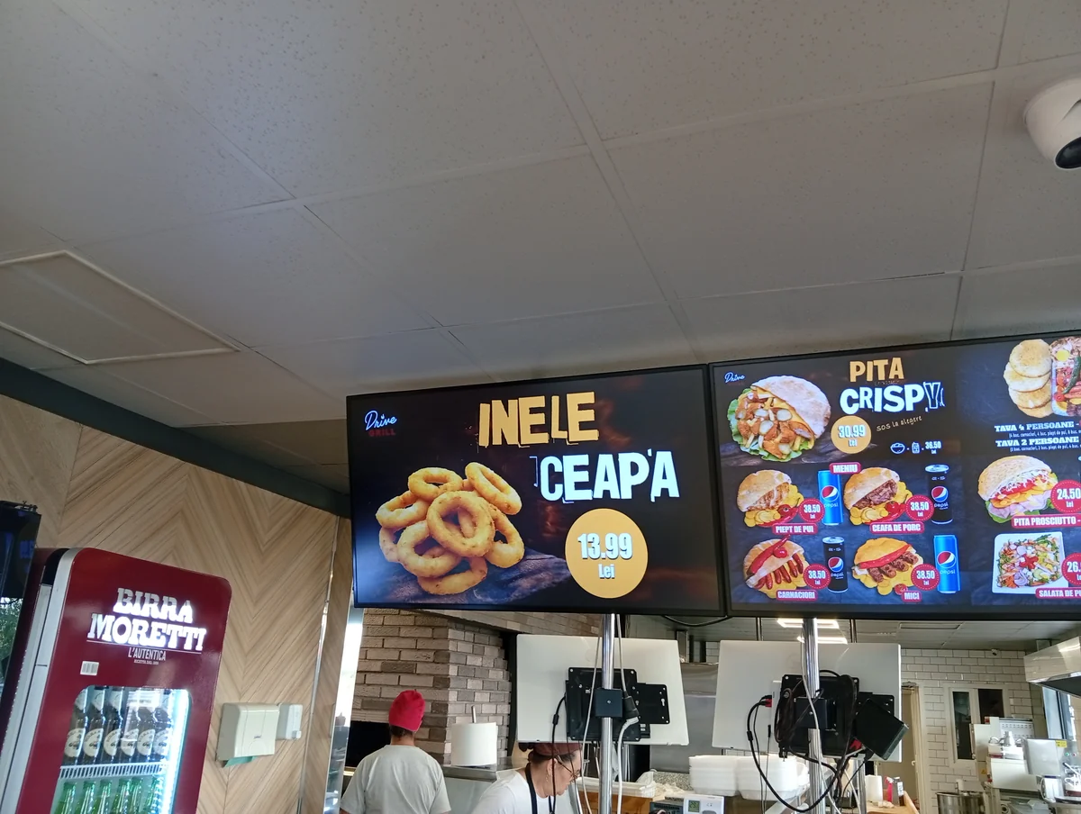 Drive Grill Craiova menu screen advertising onion rings at 13.99 lei, the kitchen and counter below, 22 September 2026