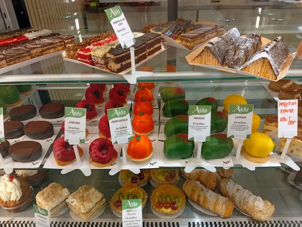 Aida bakery — chocolate croissants and pistachio-glazed croissants, both 16 lei each; apple tart and sweet-cheese tart 15 lei each; butter and jelly biscuits 84 lei a kilo. September 2026