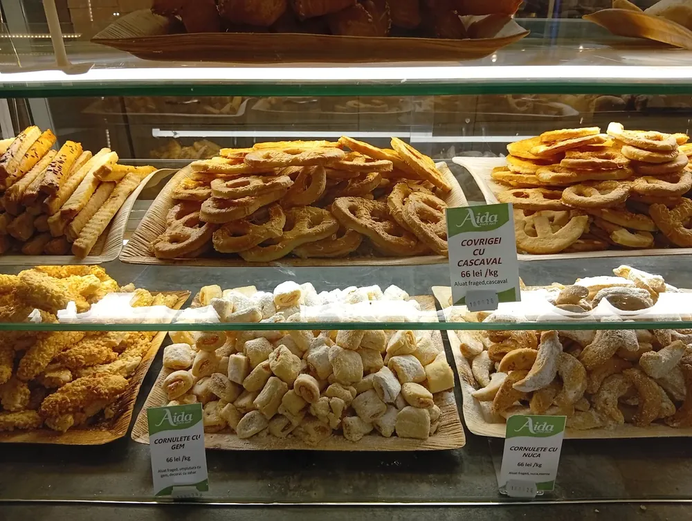 The cake counter at the same bakery — marzipan fruit mousse cakes at 24 lei each, mango 27, house mini-cakes 96 lei a kilo, cremșnit 15, fruit tart 14. September 2026