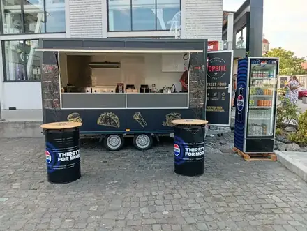 The dark TopBite street-food trailer on the cobbled plaza beside Electroputere Mall in Craiova