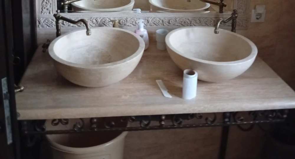 Twin stone basins under the carved mirror, bronze taps on an ironwork stand